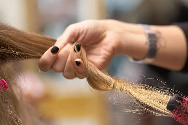 Una ciocca di capelli biondi lunghi tra le dita della parrucchiera, con la spazzola tonda