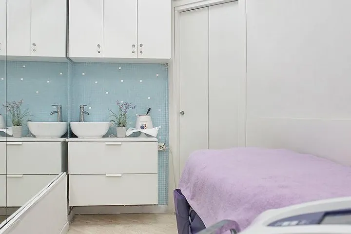 La cabina con i lavabi bianchi, le piastrelle azzurre e il lettino lilla