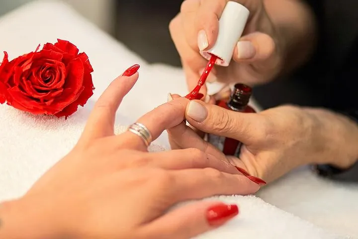 Manicure: smalto rosso steso con cura, accanto a una rosa rossa